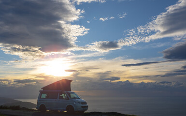 Fototapeta na wymiar Camper standing on mountain at sunset in front of the ocean