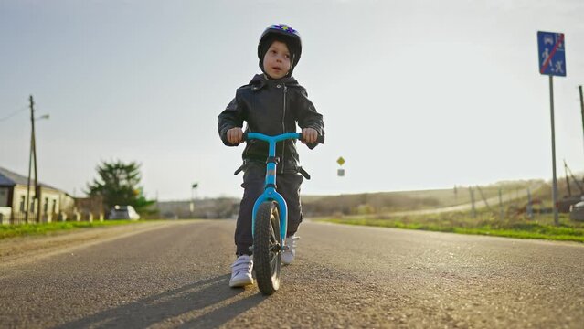 Cute little boy child wearing safety helmet learning to ride first balance bike in sunny day. Happy boy riding bike, having fun outdoors on sunset time. Active sport family concept. Slow motion 120fps