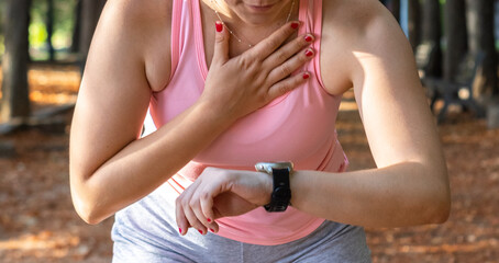 Athlete tired woman watching her smart watch in a park. Sporty young woman watching the clock in a park. Concept of sporty woman watching the smart watch in a park