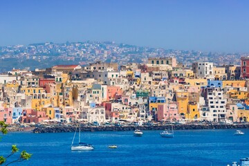 Procida in sunny summer day. Colorful houses, cafes and restaurants, fishing boats and yachts in Marina Corricella, blue sky and azure sea, Procida Island, Italy.
