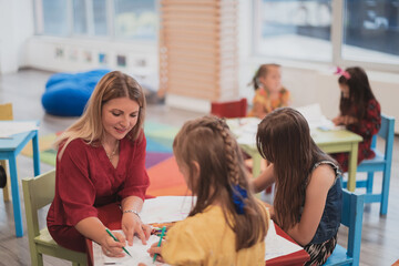 Creative kids during an art class in a daycare center or elementary school classroom drawing with female teacher. 