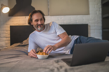 Man resting after work and eating snacks while watching something online