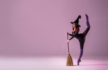 ballerina on pointe shoes in a black witch costume in a hat and with a broom is dancing on the roof...