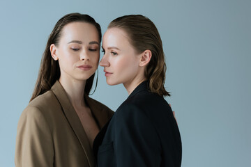 young lesbian couple in beige and black blazers standing isolated on grey.
