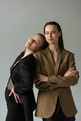 sensual lesbian woman with closed eyes leaning on girlfriend standing with crossed arms isolated on grey.