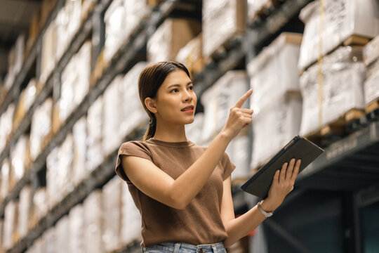 Young female manager worker checklist manage parcel box product in warehouse. Asian woman supervisor using tablet working at store industry. Logistic import export concept.