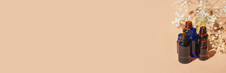 Open amber, blue and transparent bottles without cap with serum or essential oil with white flowers.