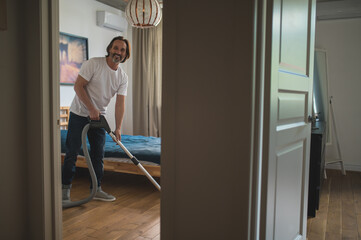 Man in white tshirt doing vacuum cleaning and looking involved
