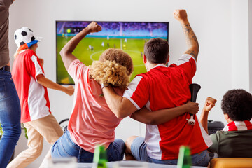 Friends cheering and celebrating while watching football on TV - obrazy, fototapety, plakaty