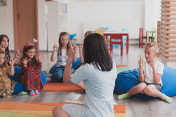 A happy female teacher sitting and playing hand games with a group of little schoolchildren