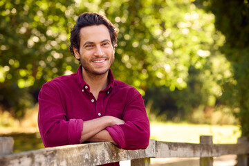 Portrait Of Smiling Casually Dressed Mature Man Leaning On Fence On Walk In Countryside
