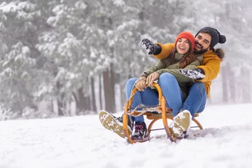 Fotobehang Couple sitting on sled and sliding down the hill while on winter vacation © Impact Photography