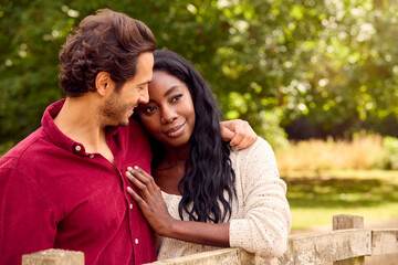 Loving Mixed Race Couple Leaning On Fence On Walk In Countryside