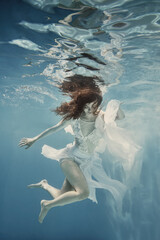 A girl with dark hair in a white dress swims underwater as if in weightlessness
