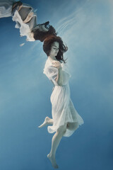 A girl with dark hair in a white dress swims underwater as if in weightlessness