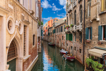 Boats near a vintage brick wall on the water surface of a narrow canal street in Venice, reflections of old houses with windows on a Venetian street, Venice canal on a sunny day