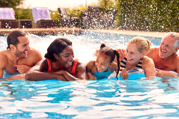 Smiling Multi-Generation Family On Summer Holiday Relaxing In Swimming Pool On Airbed
