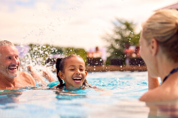Grandparents Teaching Granddaughter To Swim On Family Summer Holiday In Pool