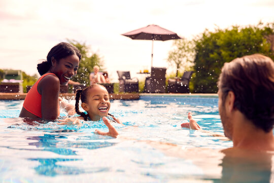 Smiling Mixed Race Family On Summer Holiday Having Fun Splashing In Outdoor Swimming Pool