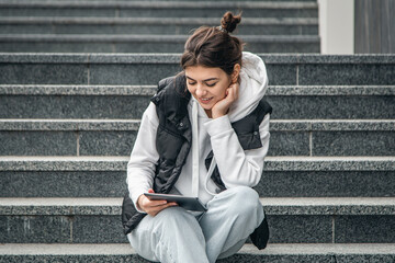 A young female student stands with a digital tablet in her hands outside.