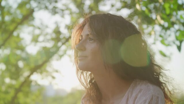 Pivoting around portrait of a young adult curly caucasian woman looking at camera with lens flare