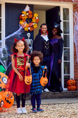 Portrait Of Family Dressed Up For Halloween Outside House Ready For Trick Or Treating