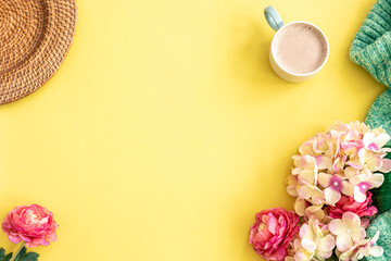 Cup of coffee, flowers and knitted element on yellow background, flat lay.