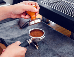 Barista cafe making coffee with manual presses ground coffee using tamper on the wooden counter bar...