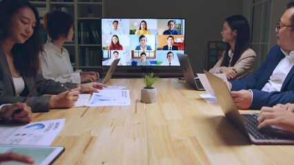 Business people group remote meeting with colleagues via video call conference virtual meeting on tv screen in office at night - Powered by Adobe