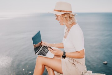 Digital nomad, Business woman working on laptop by the sea. Pretty lady typing on computer by the sea at sunset, makes a business transaction online from a distance. Freelance, remote work on vacation