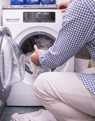Mature Man Loading clothes and linen in washing machine. Doing laundry at home