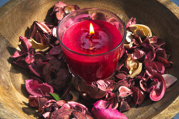 Close-up, burning red candle among rose petals.