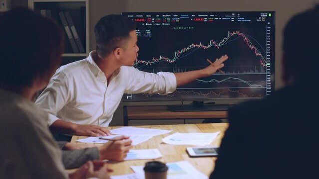 Asian businessman talking about stock market investment and graph from tv screen with broker trader, giving money plan management and analysis