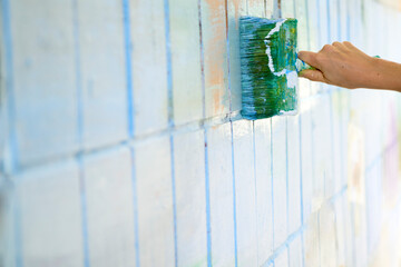 Painting a tiled wall. Green and blue paint brush on white wall