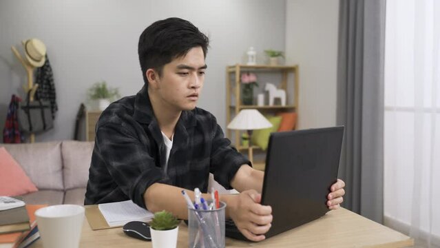 furious asian male is cursing angrily feeling annoyed with an unexpected error on computer device while working from home on a project in the living room