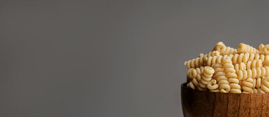 Gluten Free Cornmeal Pasta in wooden Bowl. Spiral Raw Macaroni from Blend of Corn and Rice flour. Close Up, Front View. Uncooked Bucati Pasta. Food Background. Horizontal banner with space for text