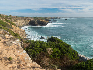 Fototapeta na wymiar View over coastline with cliffs and rocks in the ocean towards village Vila Nova de Milfontes. Fishermans hiking trail at wild Rota Vicentina coast