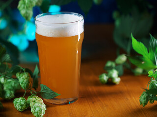 Beer glass of craft IPA on a wooden table, green hop cones