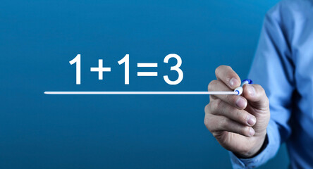 Male hand writes 1+1=3. Synergy