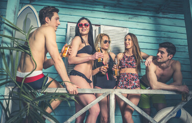 Group of five friends celebrating in their summer beach house. Party people spending a vacation day in their bungalow in a tropical village in front the ocean