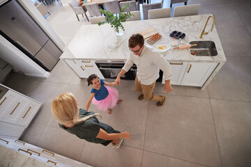 Family, children and dance with a girl and her parents dancing together in the kitchen of their home. Smile, fun and playful with a female child, her mother and father feeling happy in their house