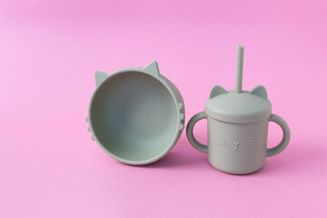 Modern pastel color set of silicone sippy cups with straws  and bowl on pink background. Baby tableware, first feeding, serving concept.