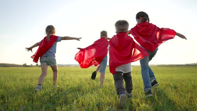 Group of children dressed as superhero. Children play in the park. Kid together in the summer in nature. Family in red suits is a childhood dream. Joyful funny kid play on the green grass in meadow.
