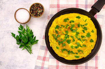 omelette with parsley in a pan on a gray background top view