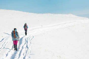 two girls with backpacks walk along a path in the winter mountains. hiking in the mountains.