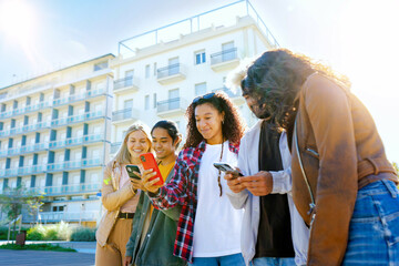 Fototapeta na wymiar Group of multiracial friends loocking mobile phone outside - College teenagers using smaprtphone at campus univeristy- Youth Concpet with guys and girls having fun- Concept Social media 