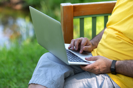 A man working and typing on laptop keyboard while sitting in the park