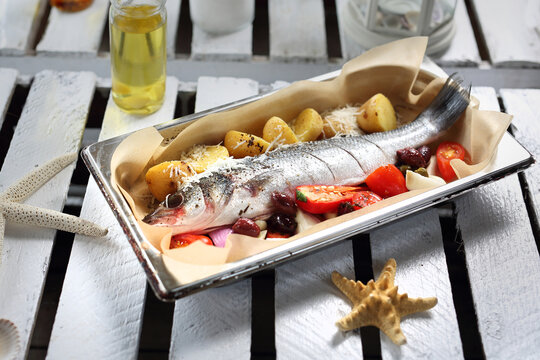 Raw sea bass with vegetables in a baking dish, top view. Baking fish in a sheet pan lined with parchment paper.