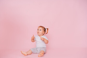 Cute little happy girl looking and pointing up on a pink background, advertising children's products