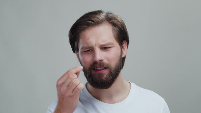 Dermatology concept. Portrait of bearded caucasian unhappy man notices pimple acne on his face getting stressed. Skincare problems.